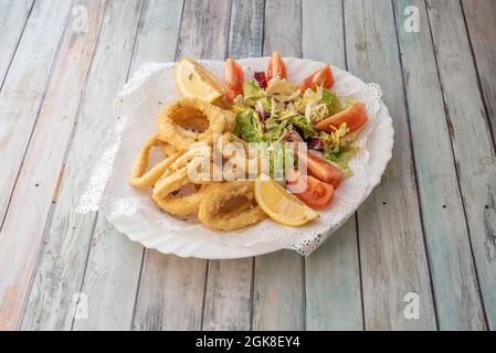 Tapa spagnola di calamari in pastella con insalata di lattuga e pomodoro e spicchi di limone su piatto bianco Foto Stock
