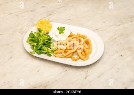 Vassoio rotondo di calamari andalusi con alcuni germogli di lattuga di agnello, limone e maionese su un tavolo di marmo Foto Stock