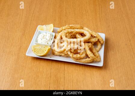 Calamari andalusi fritti in un vassoio rettangolare bianco servito in un ristorante di tapas con maionese e limoni Foto Stock