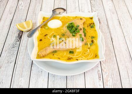 Tipico brodo di pollo peruviano con gamba di pollo vecchia, verdure assortite, spaghetti, uova sode e un sacco di liquido bollente su un tavolo leggero Foto Stock