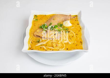 Tipica ricetta peruviana di brodo di pollo con spaghetti, uova bollite e zampa di gallina con abbondante liquido su sfondo bianco. Foto Stock