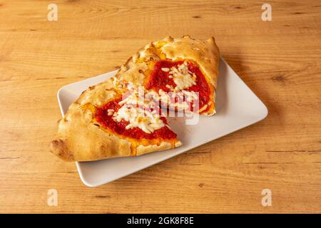 delizioso calzone ripieno di prosciutto, formaggio e pomodoro cotto in forno a pietra su un tavolo di legno Foto Stock