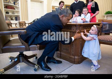 Il presidente Barack Obama detiene la mano di Lincoln Rose Pierce Smith, figlia dell'ex vice segretario alla stampa Jamie Smith, presso l'ufficio ovale, il 4 aprile 2014. Guardando dall'altro lato del Resolute Desk sono Elsa Smith, 5 anni, e Sage Smith, 6 anni, cugini di Lincoln. (Foto ufficiale della Casa Bianca di Pete Souza) questa fotografia ufficiale della Casa Bianca è resa disponibile solo per la pubblicazione da parte delle organizzazioni di notizie e/o per uso personale la stampa dal soggetto(i) della fotografia. La fotografia non può essere manipolata in alcun modo e non può essere utilizzata in materiali commerciali o politici; Foto Stock