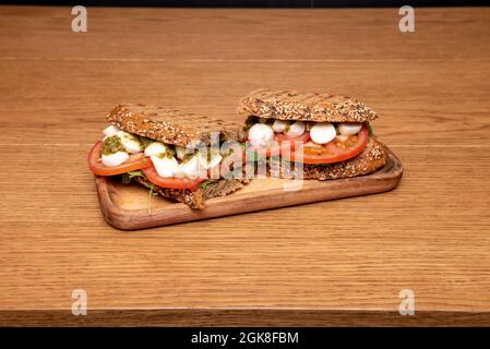 Sandwich con pane di segale e semi ripieni di insalata caprese con mozzarella, pomodoro, salsa di pesto e germogli di rucola Foto Stock