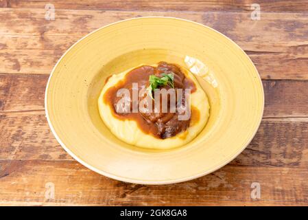 Ricetta di guance stufate su un letto di purè di patate in un piatto giallo profondo su un tavolo di legno Foto Stock