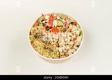 Insalata mediterranea con pollo, quinoa bianca cotta, prezzemolo tritato, pomodoro e formaggio, hummus e piselli di ceci e zucca in una ciotola di cartone per Foto Stock