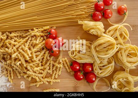 Immagine dall'alto dei pomodori ciliegini frizzanti, pasta italiana di vario tipo, tutti su un tavolo di bambù. Foto Stock