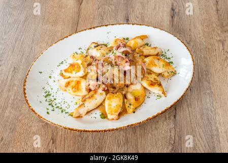 Ottima ricetta spagnola per i calamari fritti con le punte e la cipolla caramellata su un vassoio bianco con prezzemolo tritato Foto Stock