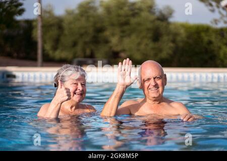 Coppia allegra che agita mentre nuotate in piscina e guardate la macchina fotografica Foto Stock