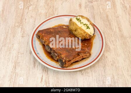 Rack di costolette in salsa barbecue guarnito con patate arrosto con buccia e burro e prezzemolo su tavola di legno Foto Stock