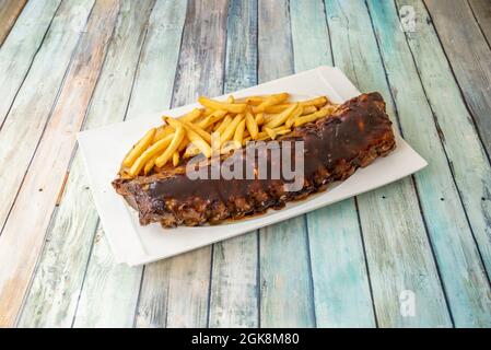 Deliziose costolette di maiale marinate con salsa barbecue guarnite con patatine fritte su un vassoio di argilla bianca Foto Stock