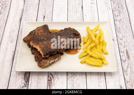 Deliziose e tenere costolette al barbecue guarnite con patatine fritte su tavola bianca in legno Foto Stock