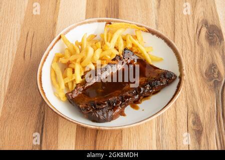 Costolette di maiale marinate in salsa barbecue con una guarnitura di patate fritte in stile nordamericano su tavola di legno Foto Stock