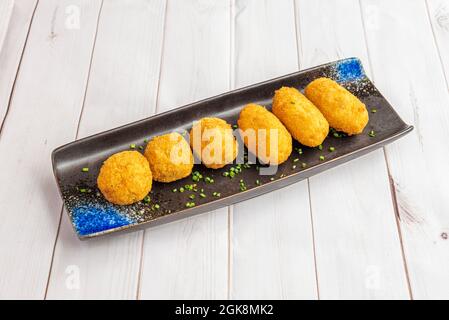 Tapa spagnola mista di boleto e crocchette di merluzzo su un piatto nero con erba cipollina tritata sulla parte superiore e su un tavolo bianco Foto Stock