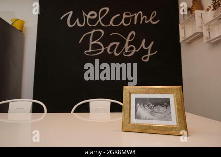 Immagine ecografica del bambino sul tavolo contro l'iscrizione Welcome Baby sulla lavagna in sala da pranzo Foto Stock