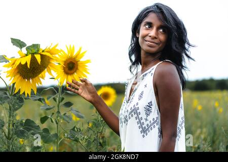 Vista laterale di anziana femmina in piedi vicino a macchia fiorente di rose rosa mentre tocca e odora fiori freschi il giorno d'estate Foto Stock