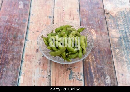 Ciotola in vetro trasparente con cialde asiatiche di edamame su tavola in legno Foto Stock