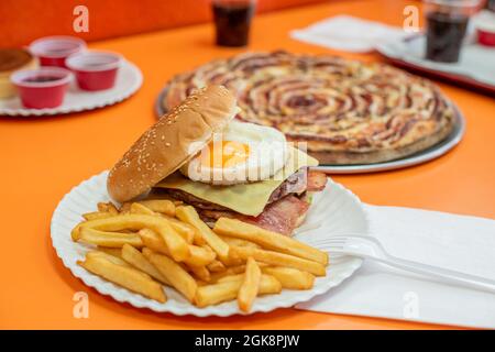 Hamburger con uova di tuorlo giallo fritte con vitello con formaggio fuso, pancetta fritta e guarnitura di patate servita in una pizzeria Foto Stock