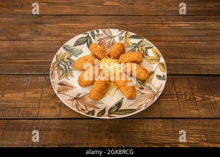 Serve crocchette spagnole ripieni di panna e prosciutto iberico accompagnato da patate di paglia su un piatto decorato con fiori su un bel legno Foto Stock