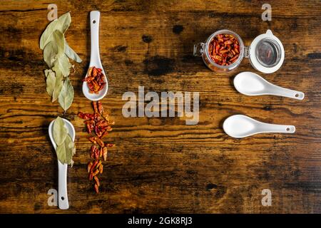 Vista dall'alto di cucchiai di porcellana bianca con cayenne e foglie di alloro su tavola di legno scuro Foto Stock
