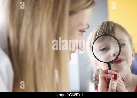 Bambina che tiene la lente d'ingrandimento vicino all'occhio accanto alla madre Foto Stock