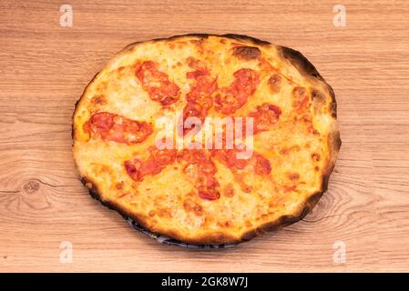 Pizza Diavola con chorizo piccante fatta con pasta di farina fine e ben bruciata intorno ai bordi su un tavolo di legno di quercia Foto Stock