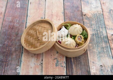 Dim sum cinese assortito all'interno di ciotola di legno per la cottura a vapore farcita con gamberi e maiale su tavola di legno Foto Stock