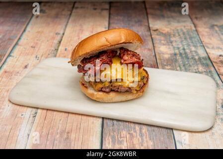 cheeseburger con doppio bacon con pancetta fritta, cheddar fuso e sottaceti su un piatto di marmo bianco Foto Stock