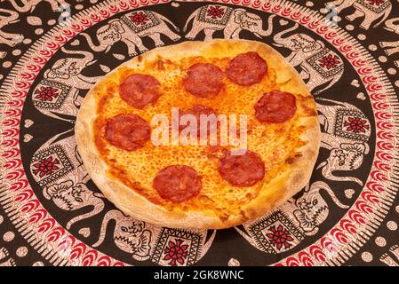 Pizza a base di crosta di grano sottile con un sacco di mozzarella e chorizo piccante su tovaglia di elefante Foto Stock