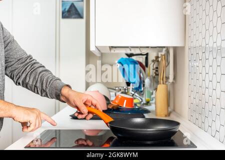 Mani dell'uomo mettere una padella per scaldare l'olio su un piano di cottura a induzione Foto Stock