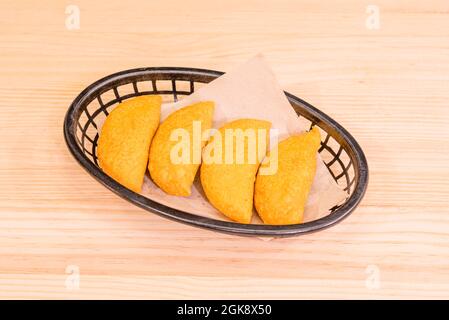 Caratteristiche empanadas colombiane di farina di mais gialla servita in un cestino di plastica nera su un tavolo di legno. Foto Stock