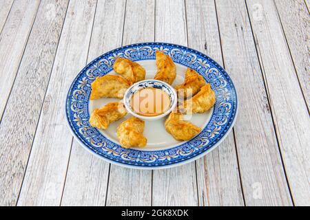 Gnocchi cinesi insolitamente preparati con pasta sfoglia fritta con olio e salsa di curry dolce per immergere su un piatto piuttosto blu Foto Stock