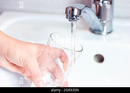 Giovane donna caucasica mano tenendo un bicchiere con acqua potabile pura versando da casa rubinetto primo piano. Foto Stock