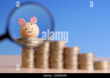 Pile di monete in euro con lente di ingrandimento davanti ad un maiale fortunato Foto Stock