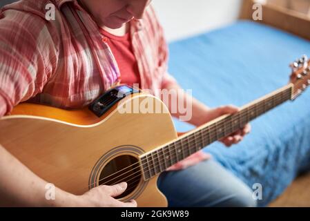 Giovane uomo irriconoscibile che sintonizza una chitarra elettroacustica, a casa. Foto Stock