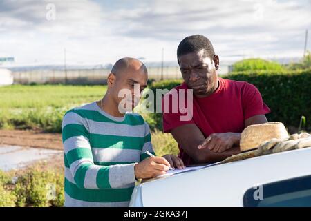 I giardinieri firmano i documenti vicino l'automobile sul campo di fattoria Foto Stock