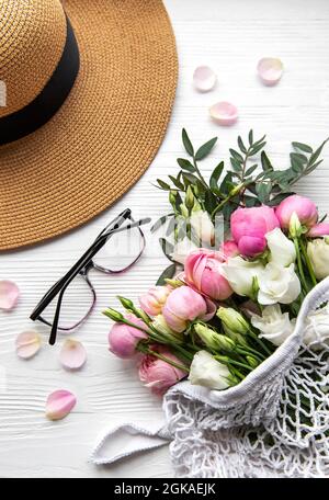 Cappello di paglia e bouquet di fiori rosa rosa su sfondo bianco. Vista dall'alto, composizione minima in stile di posa piatta. Concetto di vacanza estiva. Foto Stock