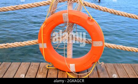 Linea di salvezza arancione e corde di mare sullo sfondo del mare e cielo blu. Funi marine e salvagente appesi su un palo. Concetto di aiuto e sicurezza Foto Stock