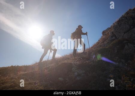 Due silhouette uomo che camminano lungo la cima della montagna con zaini da trekking si incontrano i raggi del sole e il cielo blu sfondo Foto Stock