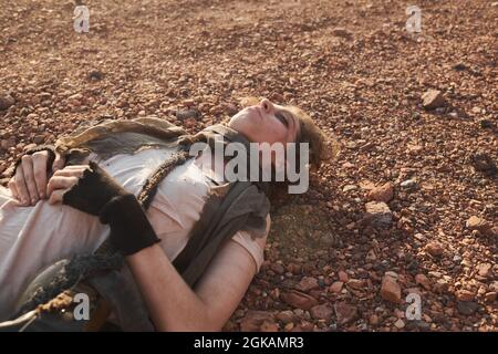 Giovane donna con volto sporco e vestiti strappati giacenti a terra con gli occhi chiusi nel deserto Foto Stock