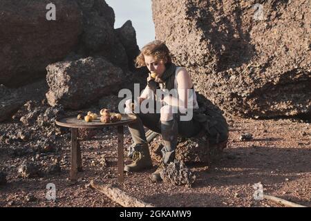 Giovane donna senza tetto seduta sulla roccia e mangiare patate all'aperto Foto Stock