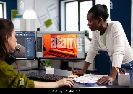 Designer multietnico che guarda computer con doppio display che lavorano insieme al progetto di gioco in startup Office. Lavoratori dei videogamer che sviluppano videogiochi digitali su pc con tecnologia moderna Foto Stock