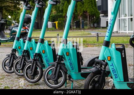 Fila di cinque escooter elettrici in piedi o e-scooter della società TIER sul marciapiede a Berlino Foto Stock