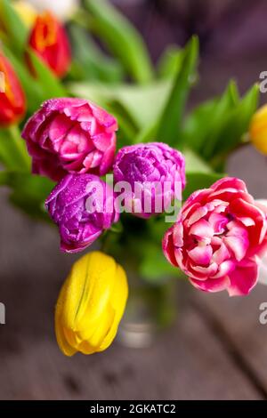Vaso con mazzi multicolore di tulipani su un tavolo di legno. Tulipano con gocce di rugiada. Messa a fuoco selettiva. Sfondo primaverile. Tulipani con gocce di rugiada Foto Stock