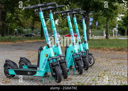 Fila di cinque escooter elettrici in piedi o e-scooter della società TIER sul marciapiede a Berlino Foto Stock