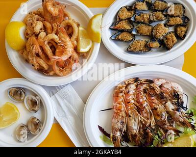 Piatto con assortimento di prodotti a base di pesce cotto in piatti di plastica su tavola arancione. Vista dall'alto delle cozze preparate in conchiglie, gamberetti e calamari servire Foto Stock