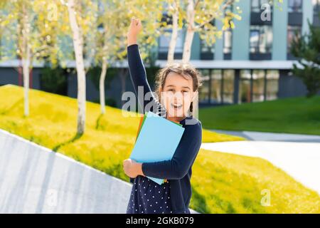 Piccola bella ragazza sorridente che tiene un libro, andando a scuola. Primo piano ritratto, infanzia. Ragazzo abbracciando un libro. Stile di vita, interesse, hobby, tempo libero Foto Stock