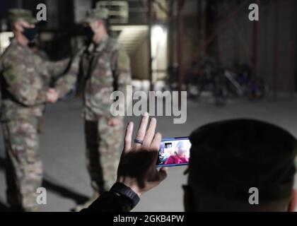 Il comandante generale del 310° comando di sostegno della Riserva dell'Esercito (Expeditionary), Briga. Il Gen. Justin Swanson, si congratula con il 310° ESC's Command Chaplain Lt. Col. David Beetham in una cerimonia di promozione informale del 1 marzo 2021 a Camp Arifjan, Kuwait, mentre la moglie e i bambini di Beetham guardano un live streaming dell'evento. Foto Stock