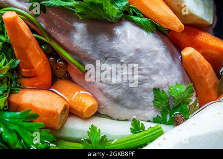 Zuppa di pollo tradizionale e lucidata (brodo) prima della cottura. Primo piano - su ingredienti crudi: Pollo, carote, sedano e prezzemolo in acqua. Pasto sano. Foto Stock