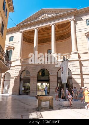 VERONA, ITALIA - 18 ago 2020: Piccola fontana in metallo in una piccola piazza con pavimento liscio e riflettente, di fronte ad un edificio storico con turisti Foto Stock